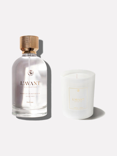 Clear glass bottle with gold foil logo of L'AVANT Collective. Gold cap on bottle. White glass candle jar with L'AVANT Collective white and gold foil label.
