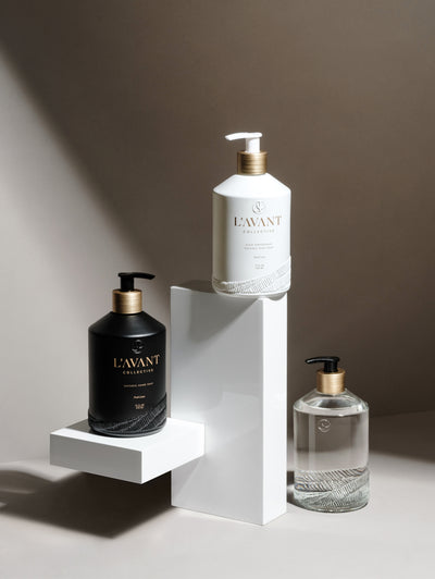 Clear glass custom bottle with brush gold neck on a black pump at bottom right, white glass custom bottle with gold foil and brush gold neck on a white pump and black glass custom bottle with gold foil text with brush gold neck on a black pump on a white tee stand
