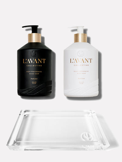 Custom glass, 16 oz black bottle with hand soap inside. White custom glass 16oz bottle wtih gold foil text "L'AVANT Collective" brushed gold neck on white pump with dish soap inside. . Clear lucite tray with LC logo etched in bottom right corner.  Tray is in front of the two bottles