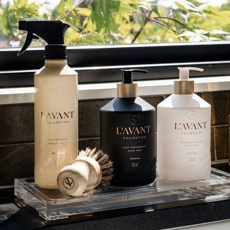 L'Avant Collective Products on a glass base next to sink and window