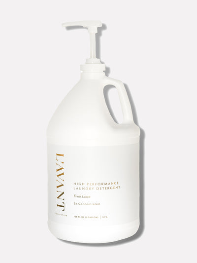 Image of a L'AVANT Collective product. A white one-gallon jug of high-performance laundry detergent labeled 'Fresh Linen, 5x Concentrated.' The jug features a sleek, minimalistic design with gold lettering and a pump dispenser.