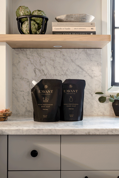 Two Black L'AVANT Collective non-toxic dish soap refill bags with fancy clear, white and black glass soap bottles alternating movements across the refills. All on a marble countertop with marble backsplash