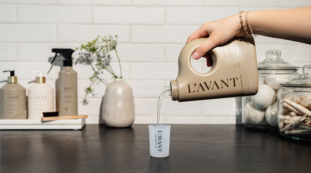 High performance laundry detergent in Ambre Santal sent being poured into a silicon laundry measuring cup on a counter in a laundry room setting.