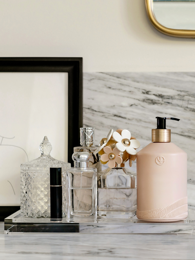 Blush pink dispenser bottle with a black pump sitting on a countertop tray with fragrance bottles