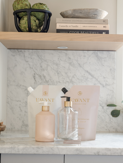 Empty blush pink and clear pump dispenser bottles on a counter with soap refill pouches