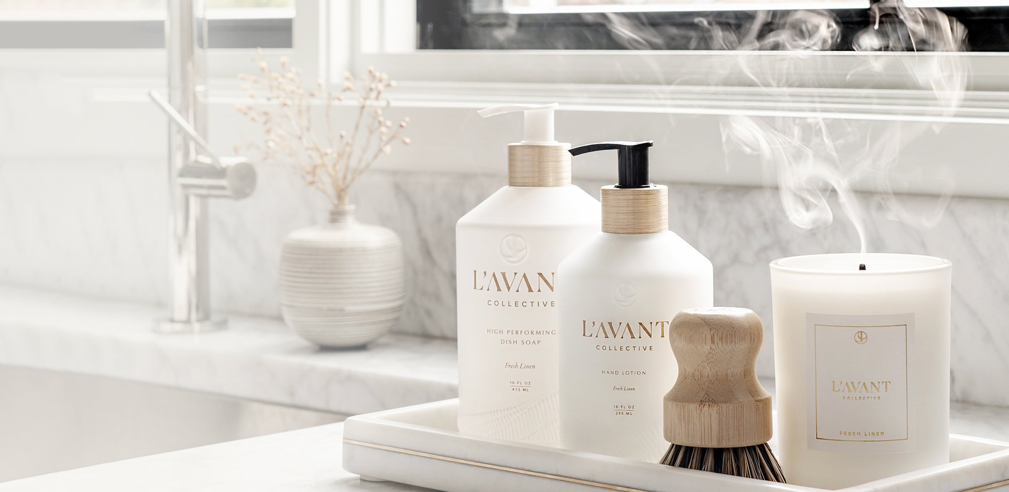 Luxurious eco-friendly hand lotion on a sinkside tray along with plant based dish soap, a natural dish scrubber, and a white scented candle