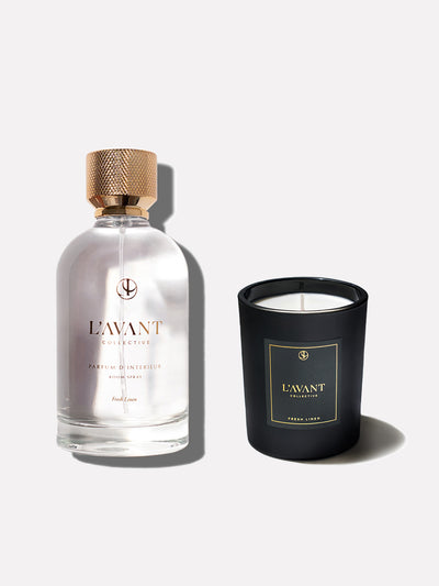 Clear glass bottle with gold foil logo of L'AVANT Collective. Gold cap on bottle. Black glass candle jar with L'AVANT Collective black and gold foil label.